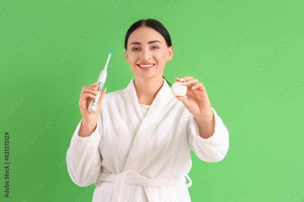 Beautiful young happy woman in bathrobe with dental floss and electric toothbrush on green background Beautiful young happy woman in bathrobe with dental floss and electric toothbrush on green background