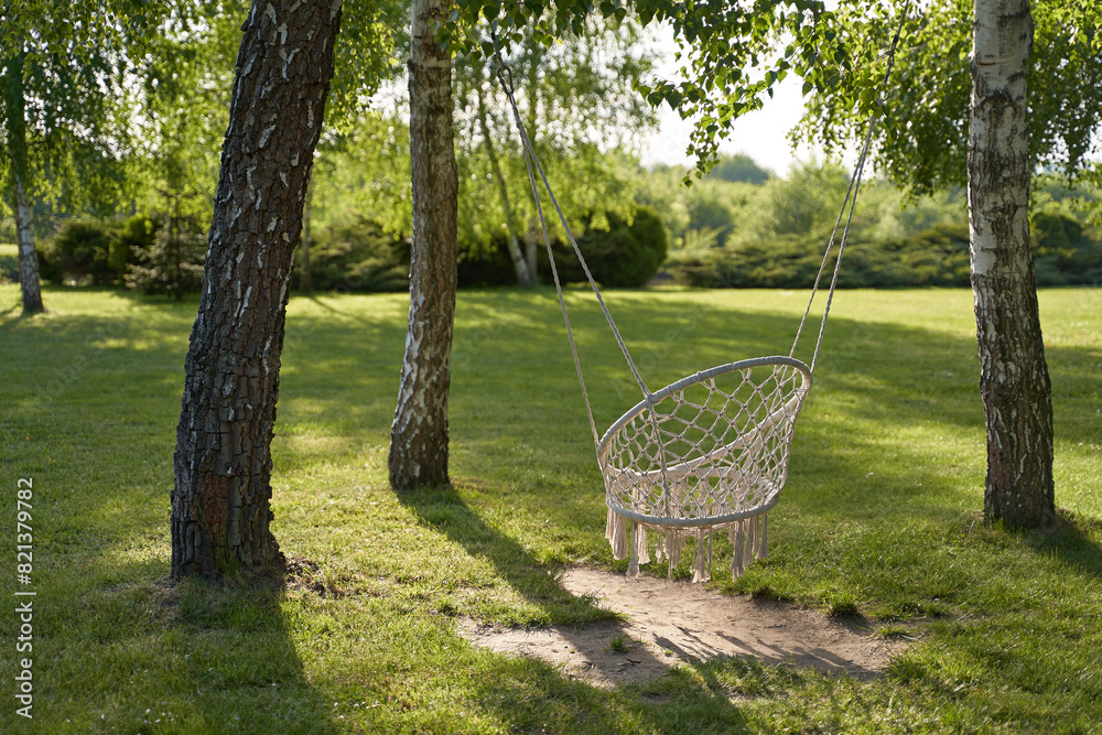 Bohemian style hammock hanging swing chair with tassels on ropes in a sunny summer or spring garden in beautiful sunlight