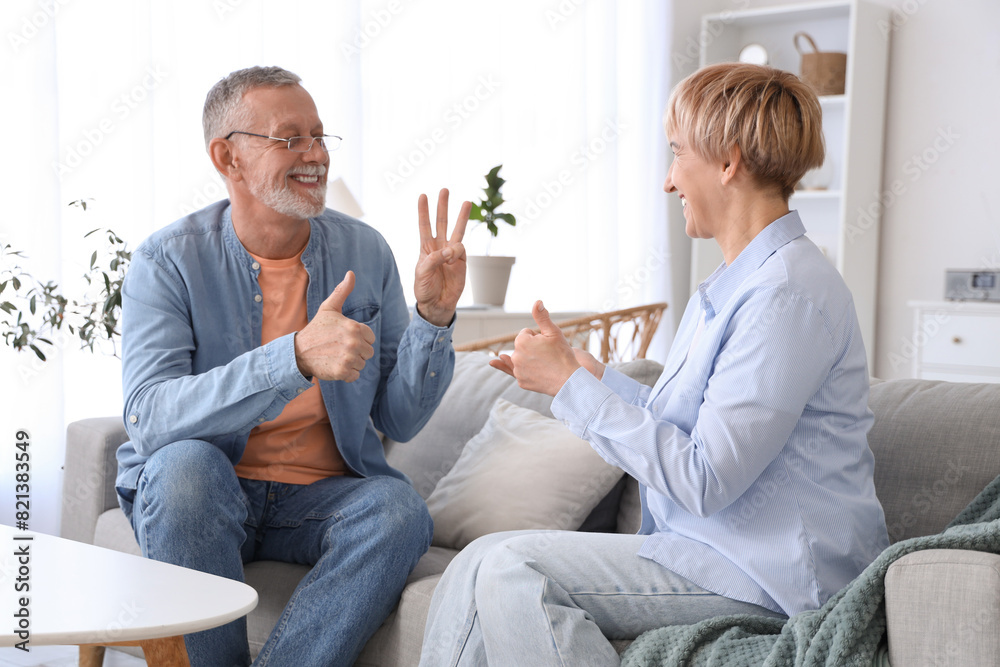 Mature deaf mute couple using sign language on sofa at home Mature deaf mute couple using sign language on sofa at home