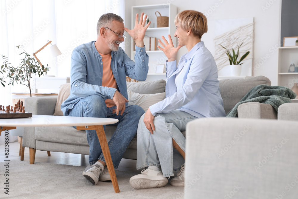 Mature deaf mute couple using sign language on sofa at home