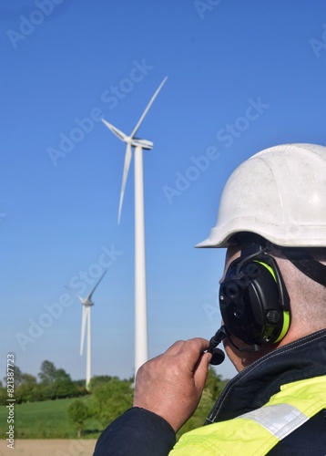 A male engineer in a hard hat and headphones controls the operation of a wind turbine.
