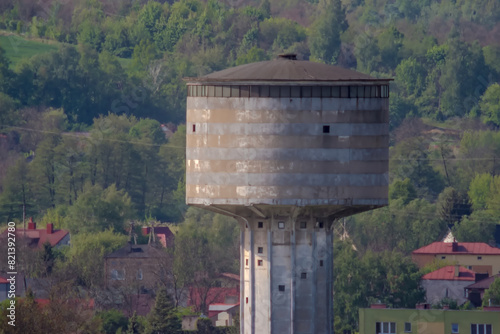 Zabytkowa betonowa wieża ciśnień w majowy poranek. Charakterystyczny punkt orientacyjny w starym hutniczym mieście (Ostrowiec) w wiosenny poranek na tle zalesionych wzgórz.
