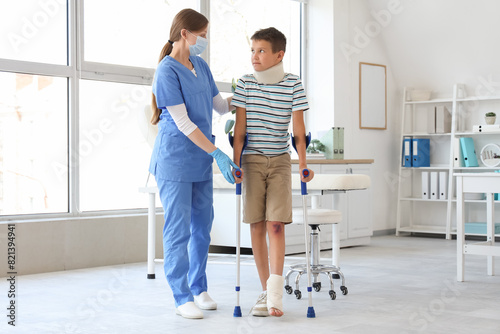 Injured little boy with crutches and doctor walking in clinic