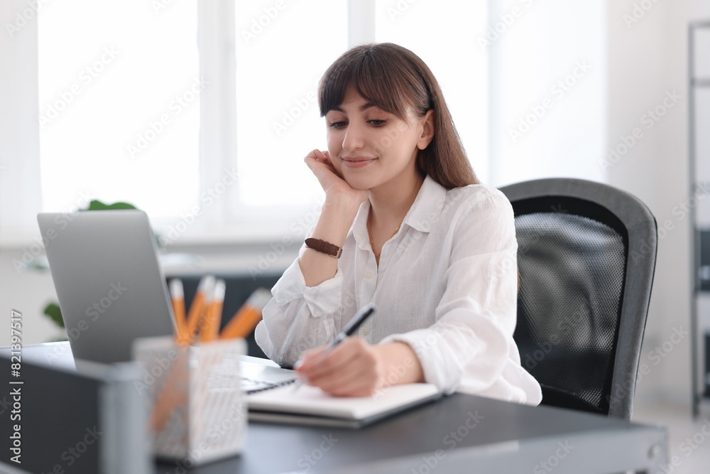Woman taking notes during webinar at table indoors Woman taking notes during webinar at table indoors