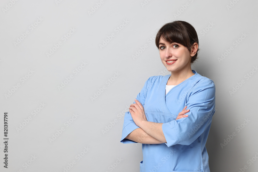 Portrait of smiling medical assistant with crossed arms on grey background. Space for text Portrait of smiling medical assistant with crossed arms on grey background. Space for text