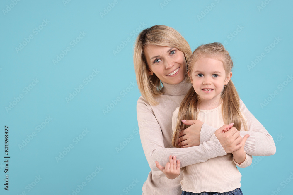 Mother hugging her happy daughter on light blue background. Space for text Mother hugging her happy daughter on light blue background. Space for text