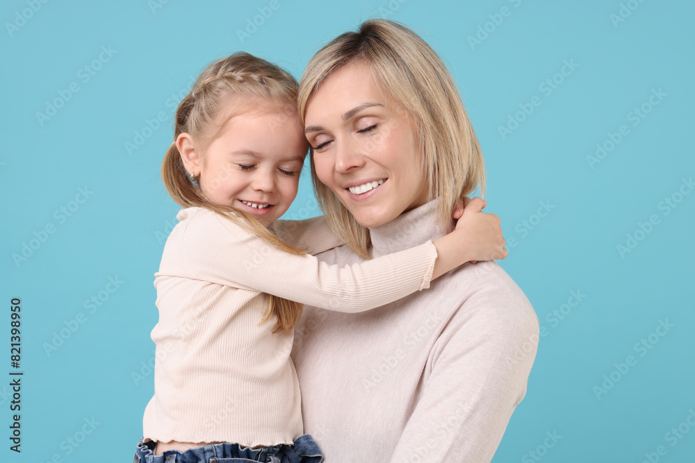 Daughter hugging her happy mother on light blue background