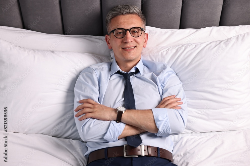 Businessman in glasses lying on bed indoors, above view