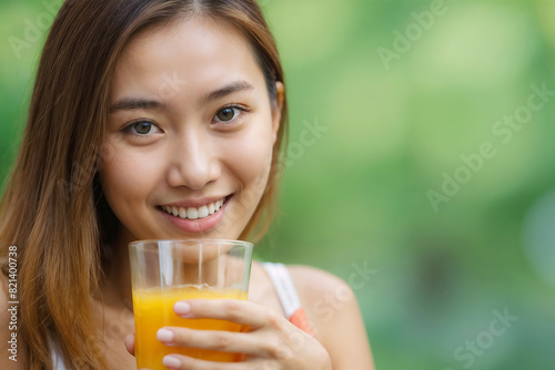 Portrait of a happy beautiful Asian girl drinking fresh orange juice on a blurred green background with copy space