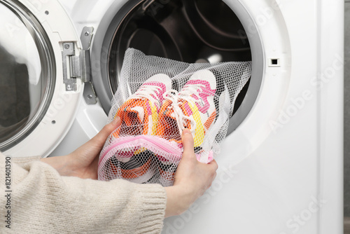 Woman putting stylish sneakers into washing machine, closeup