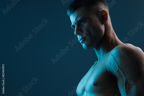Muscular model sports young man on dark background. Fashion portrait of strong brutal guy. Male flexing his muscles.