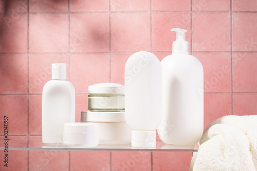 Cosmetic products at glass shelf at pink bathroom background.