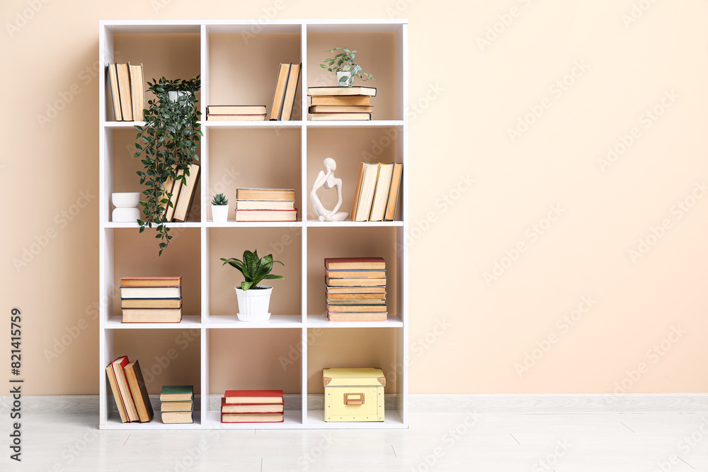 Fototapeta premium Modern shelving unit with books and home decor near beige wall