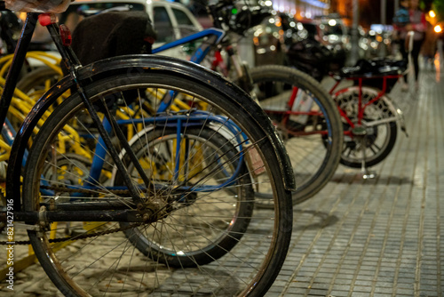 bicycles parked in a parking lot in a public square, people walking in the background
