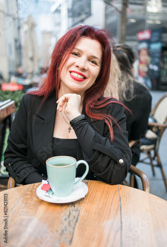 Beautiful happy millennial woman with long red hair enjoying day in a street cafe copy space