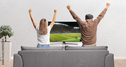 Rear view shot of an elderly man and a young woman watching a football match on tv photo