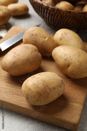 Many fresh potatoes  board and knife on grey table  closeup