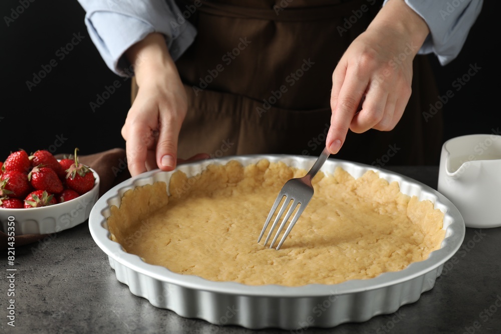 Shortcrust pastry. Woman making holes in raw dough with fork at grey table, closeup Shortcrust pastry. Woman making holes in raw dough with fork at grey table, closeup