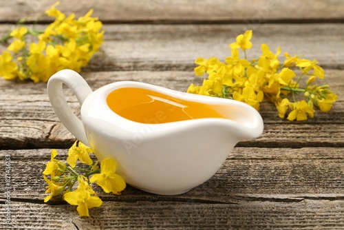 Rapeseed oil in gravy boat and beautiful yellow flowers on wooden table  closeup