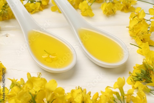 Rapeseed oil in gravy boats and beautiful yellow flowers on white wooden table, closeup