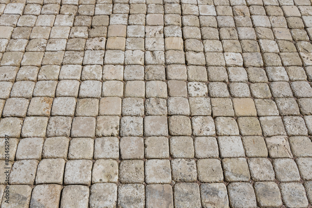  The stones are grey and appear weathered, with variations in color and texture. The pattern is consistent, with the stones laid out in a square grid.