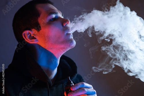 A man exhales a cloud of steam from an electronic cigarette. Vape pod mod , close-up . Colored neon light