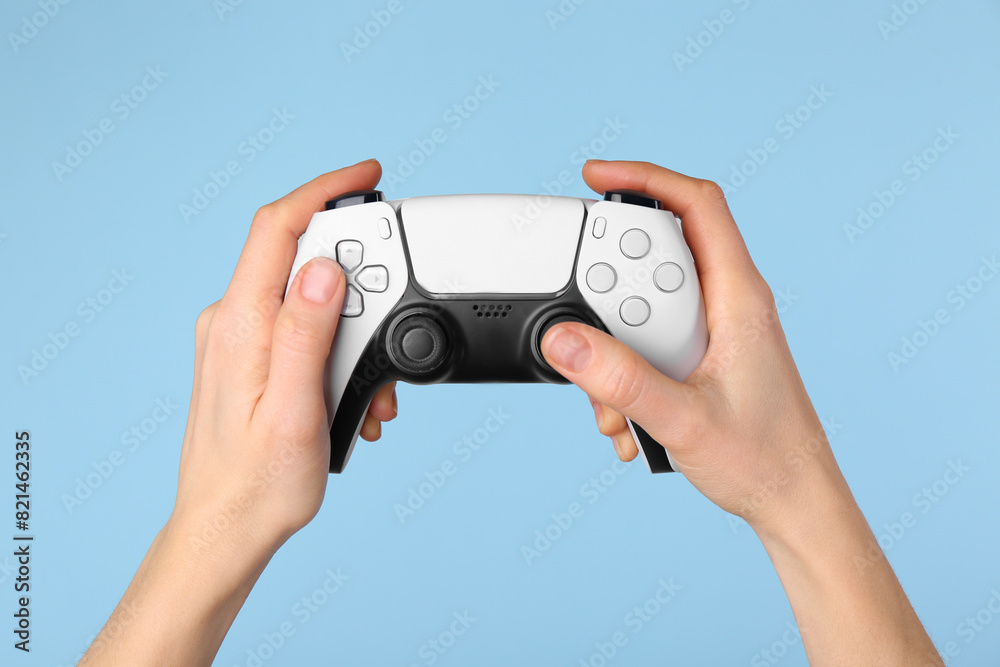 Woman using game controller on light blue background, closeup Woman using game controller on light blue background, closeup
