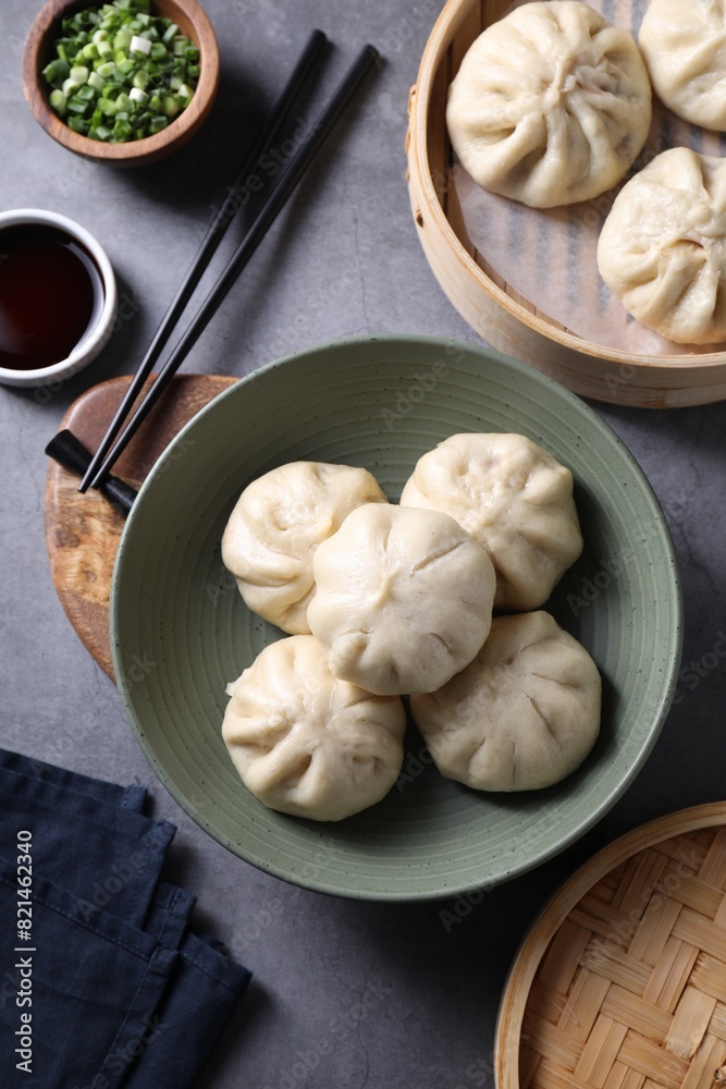 Delicious bao buns (baozi), chopsticks, soy sauce and green onion on grey table, flat lay Delicious bao buns (baozi), chopsticks, soy sauce and green onion on grey table, flat lay