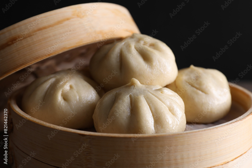 Delicious bao buns (baozi) in bamboo steamer on black background, closeup Delicious bao buns (baozi) in bamboo steamer on black background, closeup