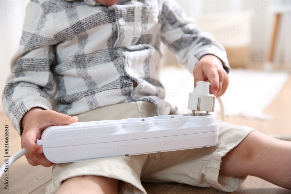 Fototapeta premium Little child playing with power strip and plug on floor indoors, closeup. Dangerous situation