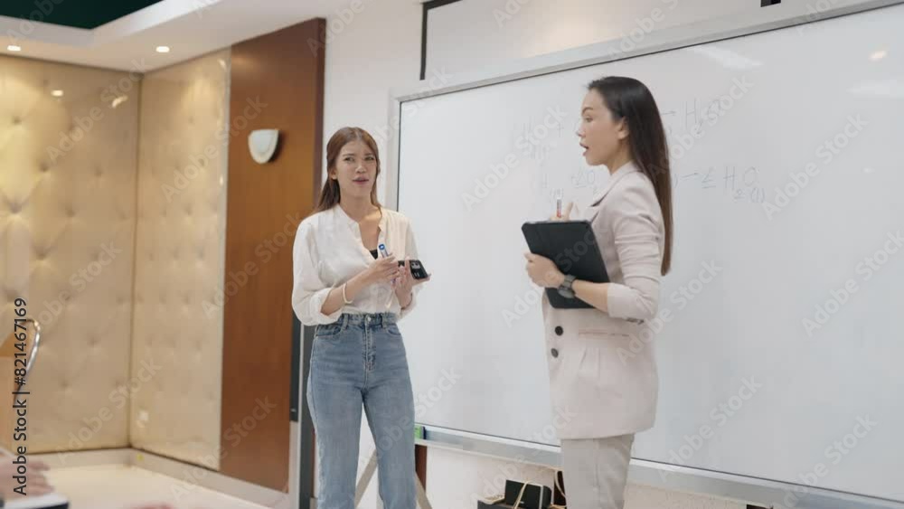 Two women are standing in front of a white board, one of them is writing on it. Scene is professional and focused, as the women are likely discussing a work-related topic Two women are standing in front of a white board, one of them is writing on it. Scene is professional and focused, as the women are likely discussing a work-related topic