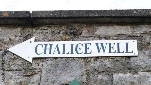 A directional sign post on old brick wall for the popular tourism attraction of Chalice Well natural water spring in Glastonbury, Somerset, UK