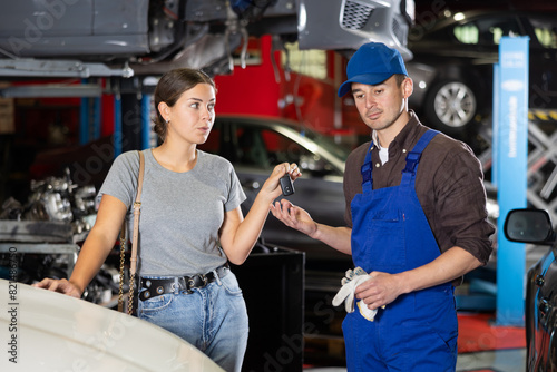 Glad young girl giving the keys of her automobile to male auto mechanic for service in car workshop
