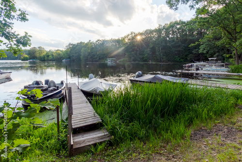 Boats are  lined up along the shore as the sun dips behind the trees on a northwoods Wisconsin lake.