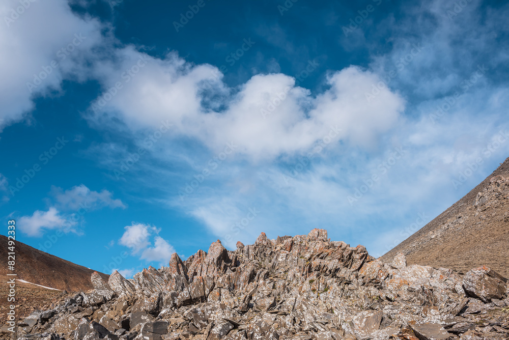 Sunlit stone hill in high mountain valley under clouds in blue sky. Pile of stones on mountain pass in bright sun. Rocky hill of round shape in sunny day. Stony mountain top in changeable weather. Sunlit stone hill in high mountain valley under clouds in blue sky. Pile of stones on mountain pass in bright sun. Rocky hill of round shape in sunny day. Stony mountain top in changeable weather.