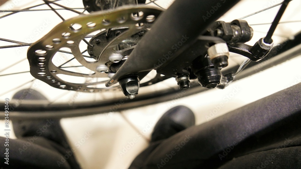 Fototapeta premium POV of a cyclist checking the bicycle's disc brake. A cyclist standing in front of a bike. A disc brake in details. A bike wheel.