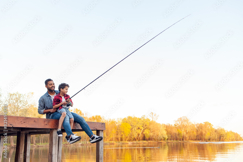 African American man and child sitting on a wooden pier holding fishing rods on the river, dad teaching his son to fish in the lake, family resting and relaxing on the weekend African American man and child sitting on a wooden pier holding fishing rods on the river, dad teaching his son to fish in the lake, family resting and relaxing on the weekend