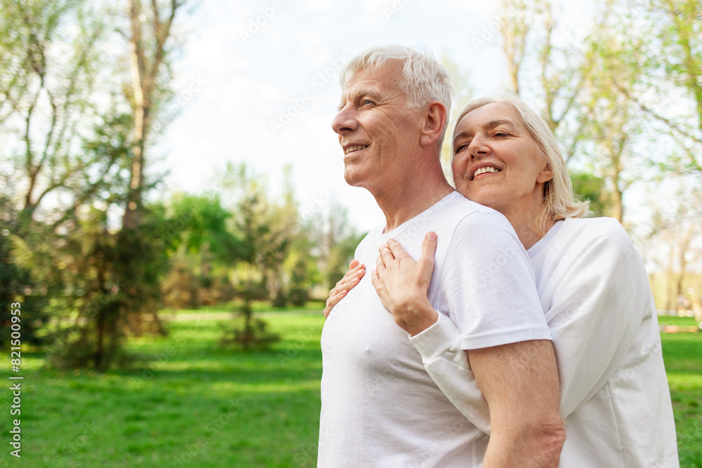 elderly couple of seniors man and woman hugging and smiling in the park outdoors, gray-haired grandparents in white T-shirts in nature elderly couple of seniors man and woman hugging and smiling in the park outdoors, gray-haired grandparents in white T-shirts in nature