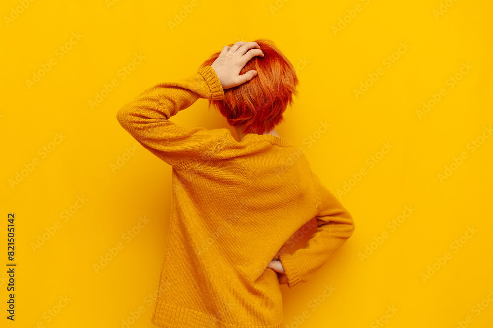 puzzled red-haired teenage boy thinks and chooses on a yellow isolated background, confused child with an orange hairstyle remembers and scratches the back of his head, rear view puzzled red-haired teenage boy thinks and chooses on a yellow isolated background, confused child with an orange hairstyle remembers and scratches the back of his head, rear view