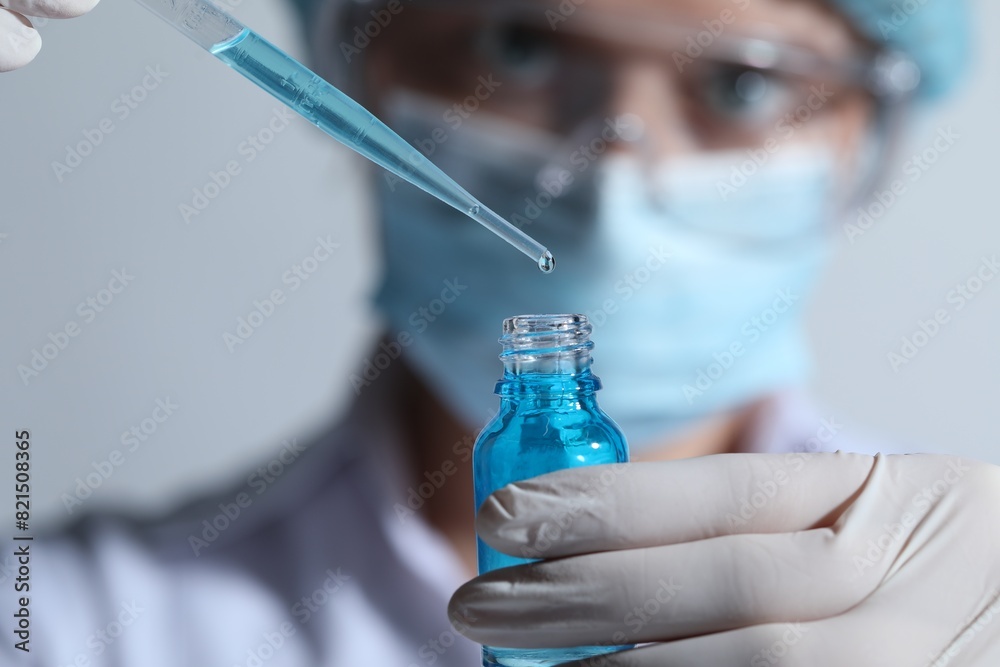 Scientist dripping liquid from pipette into glass bottle on light background, closeup Scientist dripping liquid from pipette into glass bottle on light background, closeup