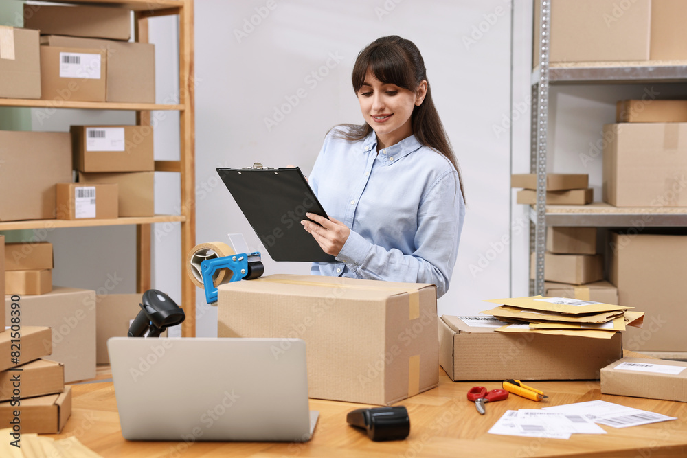 Parcel packing. Post office worker with clipboard writing notes at wooden table indoors Parcel packing. Post office worker with clipboard writing notes at wooden table indoors