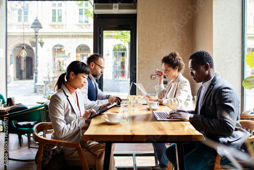 Group of businesspeople working on laptops and tablets in a cafe photo