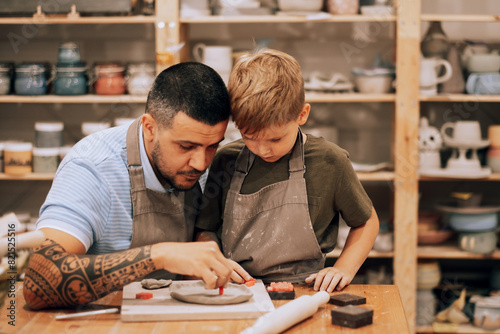 A young father and his seven-year-old son are engaged in creativity in a pottery workshop.