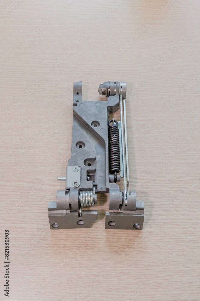 Close-up of a hinge mechanism with a bolt and spring on a light wooden surface Close-up of a hinge mechanism with a bolt and spring on a light wooden surface