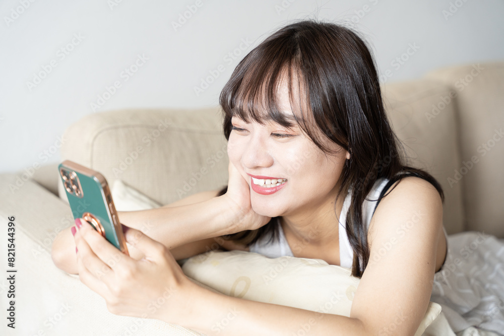 ソファに横になってスマホを見ている女性 ソファに横になってスマホを見ている女性
