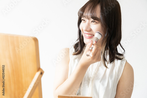 鏡を見ながらチークをブラシで塗っている笑顔の女性 photo