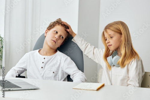 Happy children studying online with laptops and headphones at home in their cozy living room The boy and girl, siblings, are sitting at the table, fully concentrated on their elearning lessons The