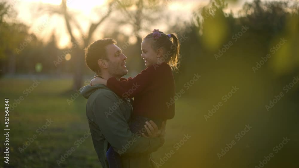 Young father holding his cute little daughter on hands in the park. Caucasian man spending autumn evening with the kid Young father holding his cute little daughter on hands in the park. Caucasian man spending autumn evening with the kid