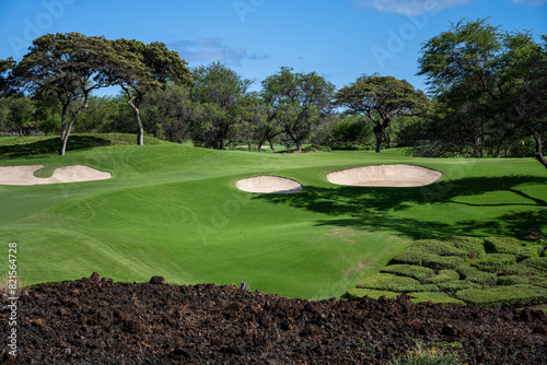 Beautiful blue sky day on the golf course, lava rock wall with fairway and sand traps, green and yellow flag around a dogleg corner, tropical golf vacation, Maui, Hawaii
 photo