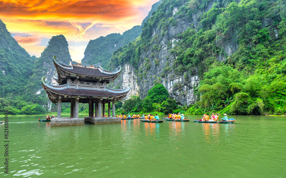 Obraz premium Ninh Binh, Vietnam - April 5th, 2024: Tourists float by boat on the river of the Tam Coc National Park Sightseeing tour to grottoes with sunset sky, Ninh Binh, Vietnam.
